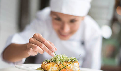 Cook decorating a plate and putting the ultimate touches - focus on foreground 